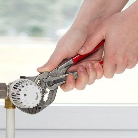 Eine Person verwendet eine Zange, um einen Heizungsdrehknopf zu befestigen